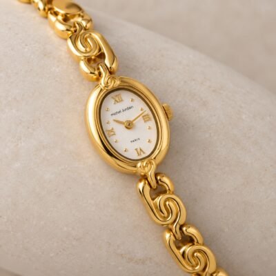 Close-up of the ivory dial and curved gold-tone bracelet links on pale stone